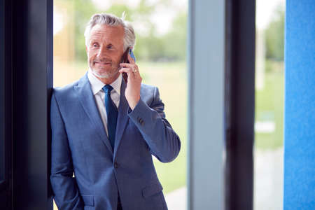 Senior Businessman CEO Chairman By Window Inside Modern Office Building Calling On Mobile Phoneの写真素材