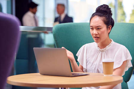 Businesswoman Having Video Call On Laptop At Table In Breakout Seating Area Of Office Buildingの写真素材