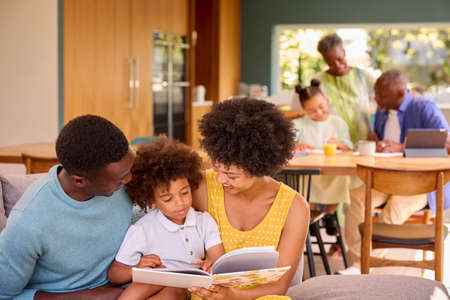 Multi-Generation Family With Parents Read Book To Son At Home As Grandparents Talk To Granddaughter