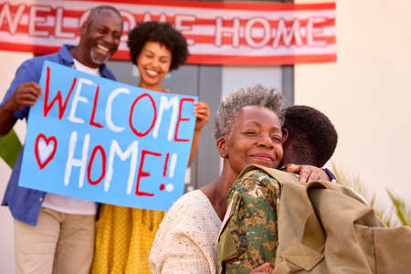 Multi-Generation Family With Parents And Wife Welcoming Army Soldier Home On Leave With Banner