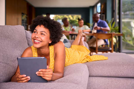 Woman On Sofa Using Digital Tablet With Multi-Generation Family Behind