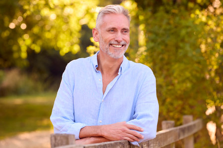 Casually Dressed Mature Man Leaning On Fence On Walk In Countryside