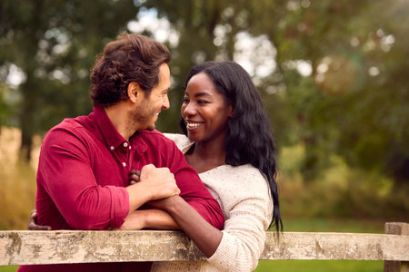 Loving Mixed Race Couple Leaning On Fence On Walk In Countrysideの写真素材