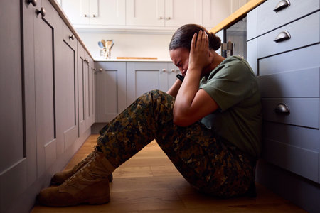 Depressed Female Soldier In Uniform Suffering With PTSD Sitting On Kitchen Floor On Home Leaveの写真素材