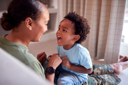 Loving Army Mother In Uniform Home On Leave Sitting On Sofa Hugging Son In Family Lounge