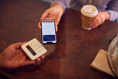 Close Up Of Customer Making Contactless Payment In Coffee Shop Using Mobile Phone