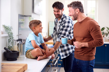 Same Sex Family With Two Dads Cooking In Kitchen With Son Sitting On Counter