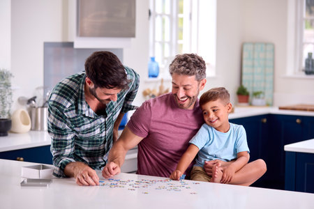 Same Sex Family With Two Dads And Son Doing Jigsaw Puzzle In Kitchen At Homeの写真素材
