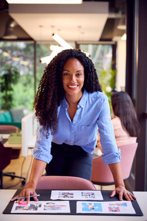 Businesswoman Standing At Table In Open Plan Office Approving Or Checking Proofs Or Design Layouts