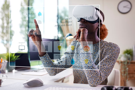 Woman Looking At Projected Screen For Smart Home Sitting At Desk Wearing VR Headsetの写真素材