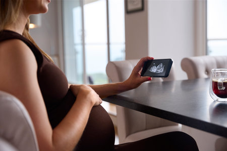 Close Up Of Pregnant Woman Looking At Phone With Ultrasound Scan Of Baby