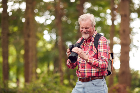 Retired Senior Man Hiking In Woodland Countryside Taking Photo With DSLR Cameraの写真素材