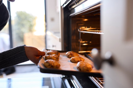 Close Up Of Woman At Home Putting Baking Tray Of Cookies In Ovenの写真素材