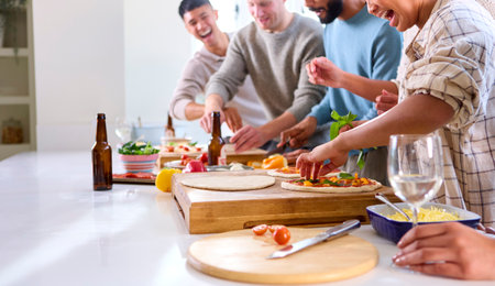 Group Of Friends At Home In Kitchen Adding Toppings To Homemade Pizzas For Party Together