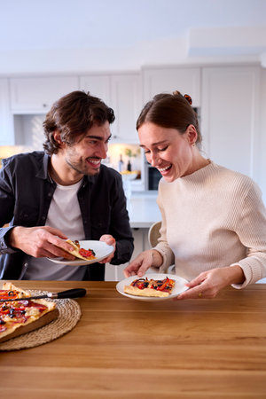 Couple In Kitchen At Home Eating Homemade Pizza Sitting At Counterの写真素材