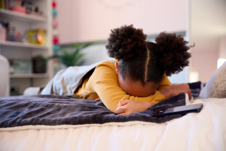 Unhappy Girl Lying On Bed At Home Being Bullied Online Via Social Media On Mobile Phoneの写真素材