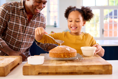 Family Shot With Father And Daughter Baking At Home In Kitchen Decorating Cake With Icing