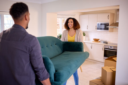 Couple Unpacking Boxes And Carrying Sofa Into New Home On Moving Day