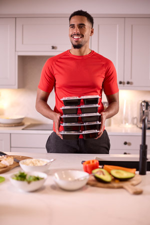 Man In Kitchen Wearing Fitness Clothing Making Batch Of Healthy Meals For Freezer In Advance
