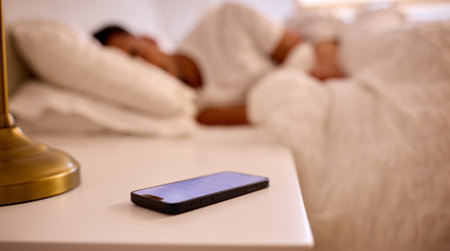 Man At Home Asleep In Bed With Alarm Going Off On Mobile Phone