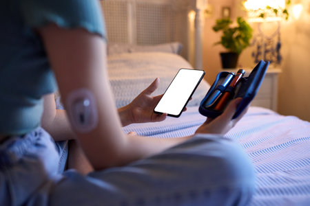 Close Up Of Diabetic Girl Sitting On Bed At Home Checking Insulin Levels On Mobile Phone App