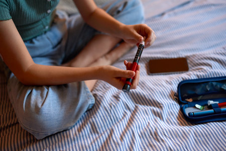 Close Up Of Young Diabetic Girl Sitting On Bed In Bedroom At Home With Kit To Check Insulin Levels