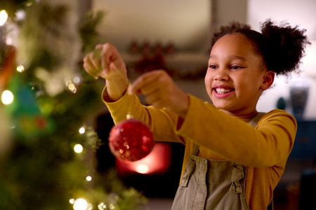Excited Girl At Home In Hanging Christmas Decoration On Treeの写真素材