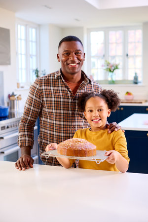 Portrait Of Proud Father And Daughter At Home In Kitchen With Homemade Cake They Have Baked Together
