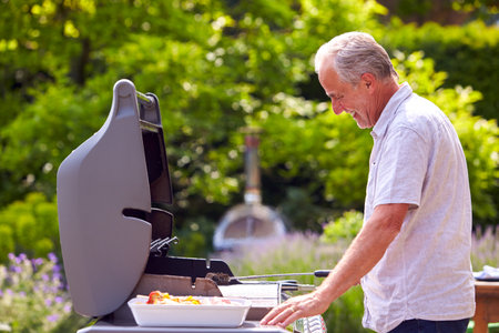Senior Man Cooking Food On Outdoor Barbeque At Homeの写真素材