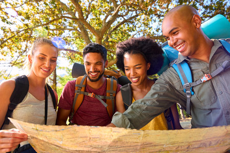 Group Of Friends With Backpacks Looking At Map On Vacation Hiking Through Forest Countryside