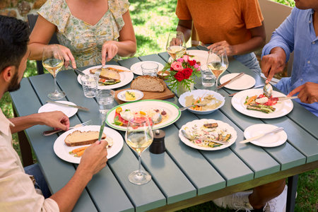 Close Up Of Friends Enjoying Outdoor Meal And Wine On Visit To Vineyard Restaurant