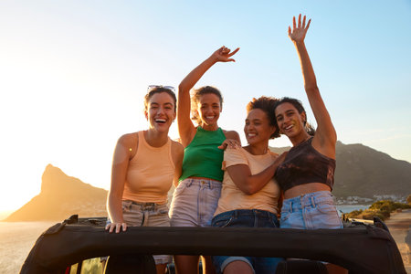 Portrait Of Female Friends Standing Up Through Sun Roof Car And Dancing On Road Tripの写真素材