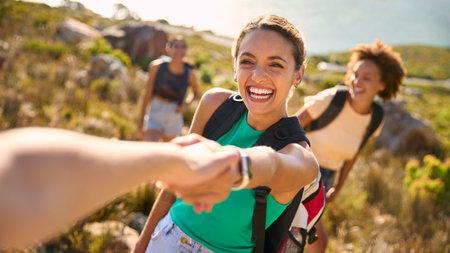 Group Of Female Friends With Backpacks Helping Each Other On Hike In Countryside On Coastal Pathの写真素材