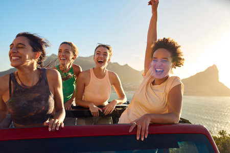 Portrait Of Female Friends Standing Up Through Sun Roof Car And Dancing On Road Tripの写真素材