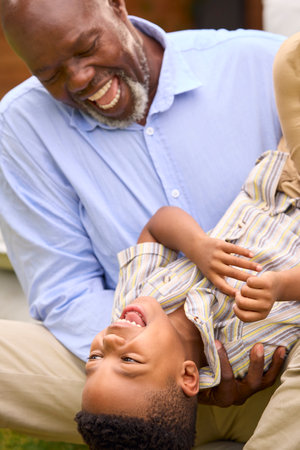 Grandfather Having Fun Playing With Grandson In Garden Holding Him Upside Downの写真素材