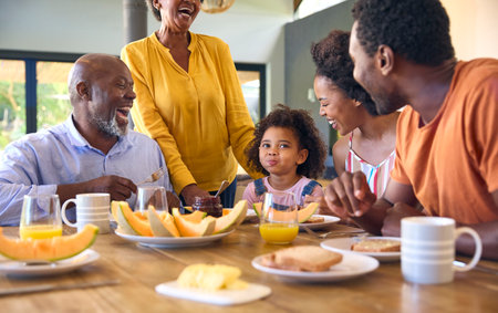Family Shot With Grandparents Parents And Granddaughter Eating Breakfast Around Table At Homeの写真素材