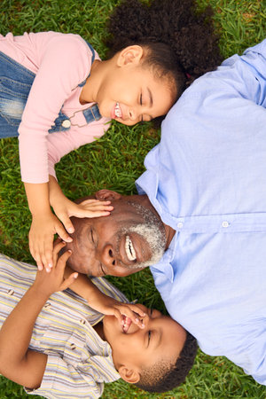 Overhead Shot Of Smiling Grandfather And Grandchildren Lying On Grass In Garden Togetherの写真素材
