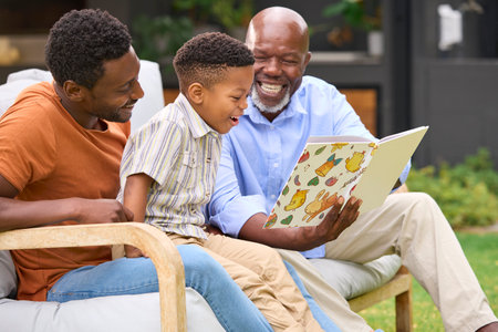 Smiling Multi-Generation Male Family Reading Book In Garden Together