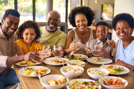 Multi-Generation Family Around Table Doing Cheers With Water Before Serving Food For Meal At Homeの写真素材