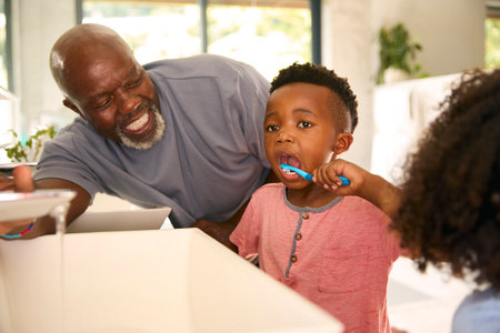 Grandfather Helping Grandchildren Brushing Teeth In Bathroom At Home Before Bedの写真素材