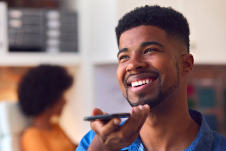 Young Smiling Businessman Working At Desk In Office Talking Into Mic Of Mobile Phoneの写真素材