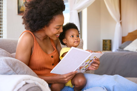Mother Sitting On Sofa At Home With Young Daughter Reading Book Togetherの写真素材