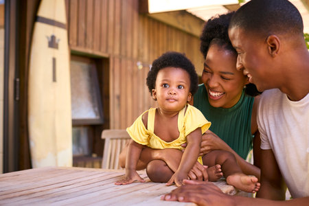 Family Shot As Parents Play With Young Daughter Sitting On Table Outdoors At Homeの写真素材