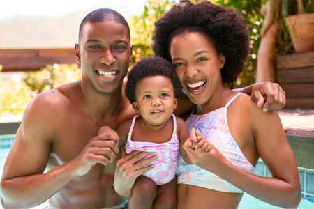 Family With Young Daughter Having Fun On Holiday In Swimming Pool Togetherの写真素材