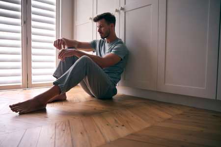 Depressed Man Suffering With Poor Mental Health Sitting On Floor At Homeの写真素材