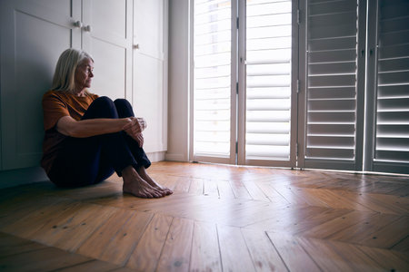 Depressed Senior Woman Suffering With Poor Mental Health Sitting On Floor At Homeの写真素材