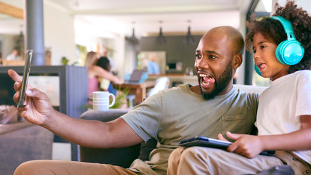 Father And Son Using Digital Tablet With Headphones At Home With Multi-Generation Family Behind