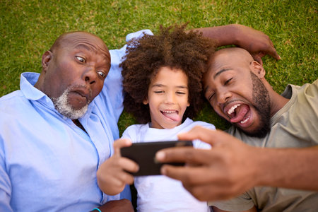 Overhead Shot Of Multi-Generation Male Family Lying On Grass Taking Selfie On Mobile Phone