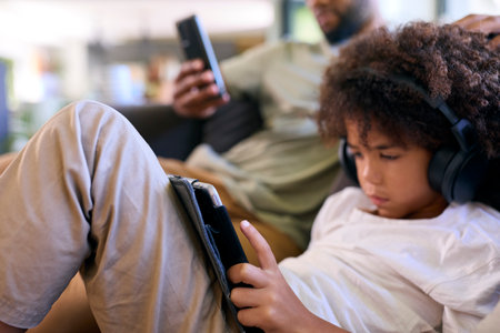 Close Up Of Father With Mobile Phone And Son Using Digital Tablet With Headphones At Homeの写真素材