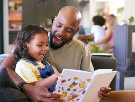 Father And Daughter Reading Book At Home Together With Multi-Generation Family In Backgroundの写真素材